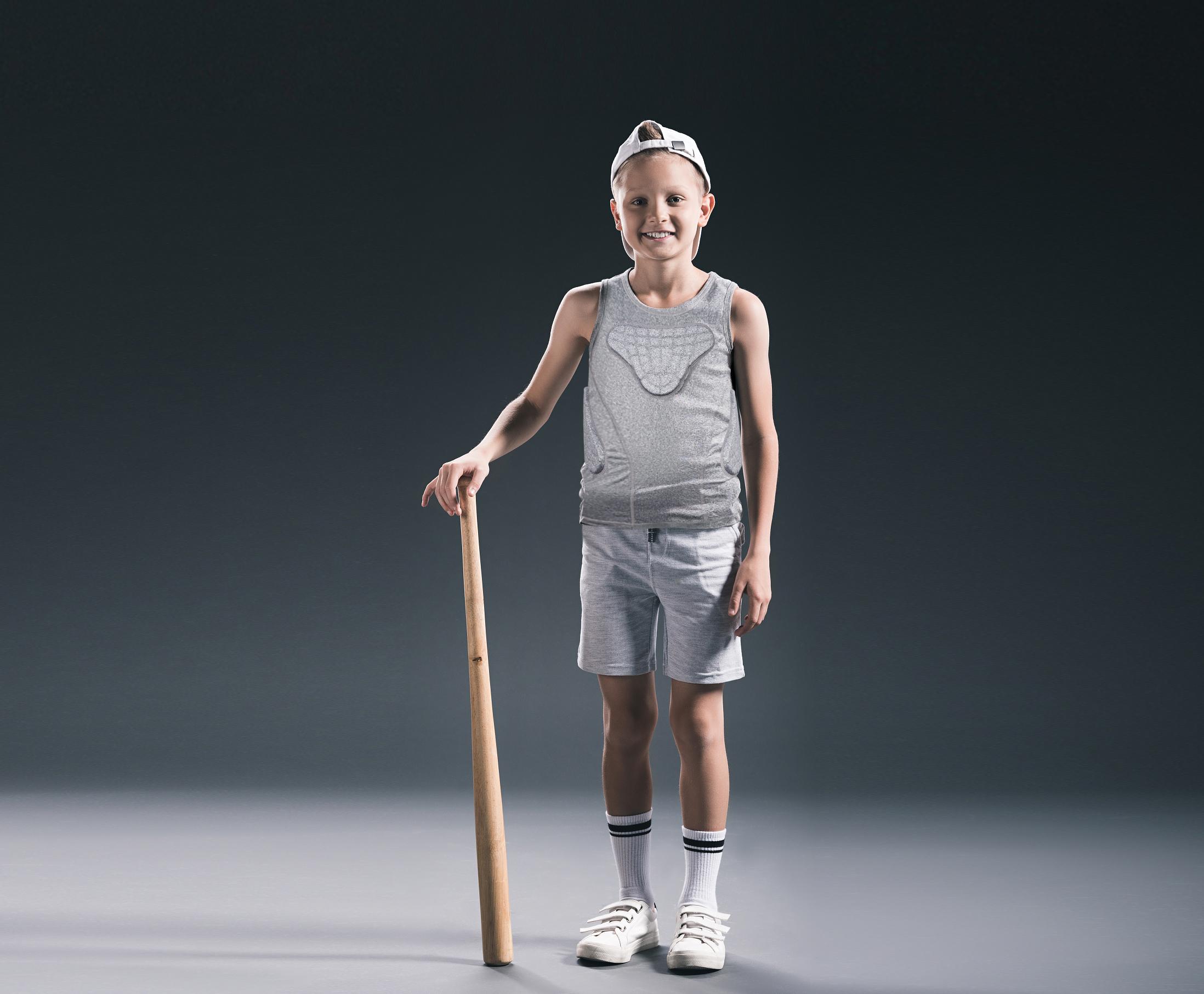 smiling boy in sportswear with baseball bat on grey backdrop